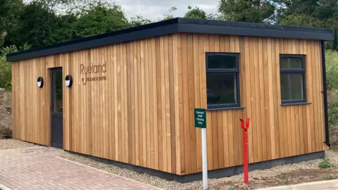 BBC / Alistair Binney A short wood building with a flat roof, with a sign on the side reading "Ryeland Research Centre".