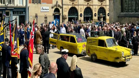 Philip Norton / BBC Surrounded by mourners is a Reliant Robin hearse painted yellow to resemble the vehicle that starred in popular TV sitcom Only Fools and Horses.
