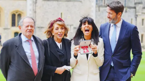 PA Media Claudia Winkleman com seu pai, mãe e marido comemorando seu MBE