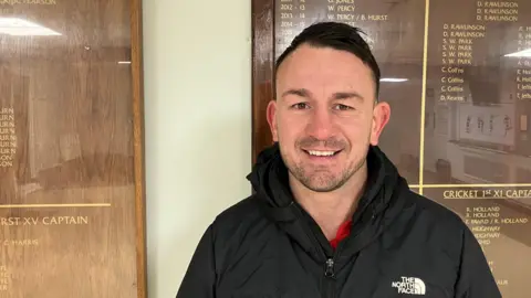 Photograph of David Kearns inside a clubhouse, in front of an honours board.