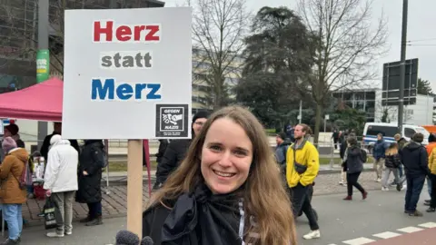 Annika, 29, waves a placard that reads in German "Herz instead of Merz"