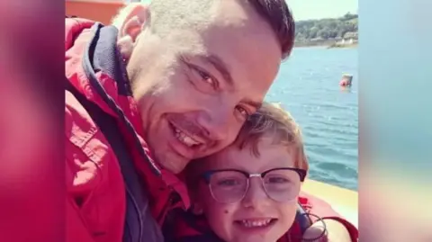 Dean and Charlie Lowe taking a selfie and smiling. Both are wearing red coats and are on a boat.