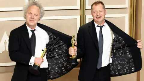 Getty Images Charlie Mackesy and Matthew Freud, winners of the Animated Short Film award for The Boy, the Mole, the Fox and the Horse, pose in the press room wearing suits in Hollywood, California in 2023.