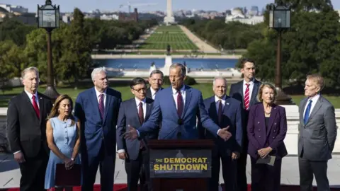 EPA Republican leaders of the US House and Senate, including Speaker of the House Mike Johnson and Senate Majority Leader John Thune, flank a podium with a sign that reads 'The Democrat Shutdown'. They are outside and the National Mall stretches out behind them. 