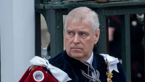 Getty Images Prince Andrew at the Coronation of the King - he is wearing a blue velvet ceremonial robe, with red and white adornments on the shoulders, with a gold medallion chain as well - he is outside and is looking off over his right shoulder