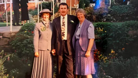 Supplied Pat with her siblings Brian and Maralyn in 1994. On the left, Pat is wearing a light-coloured hat, skirt and jacket, Brian is in the middle wearing a suit and on the right is Maralyn in a knitted purple skirt and cardigan. 