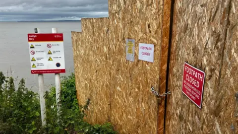Warning signs and a temporary wall blocking the unstable clifftop walk and Layde Bay