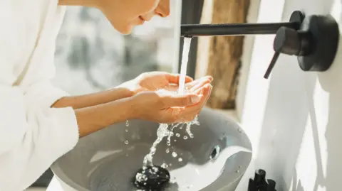 Getty Images Young woman awakening, washing and cleaning her face with splashing wate