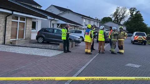 Emergency services gather in a residential street with a taped off cordon in the foreground