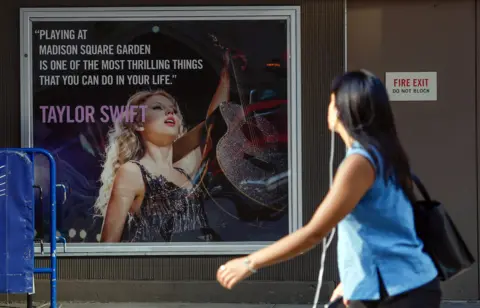 Getty Images A person walks by a poster featuring an image and quote from US singer-songwriter Taylor Swift outside Madison Square Garden in New York on July 1, 2026. 