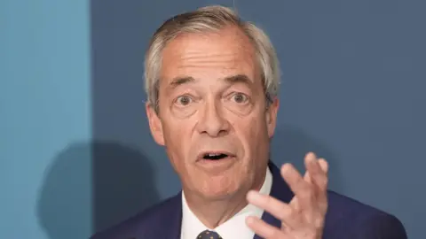 PA Media Nigel Farage speaking, with his left hand raised, at a press conference.
