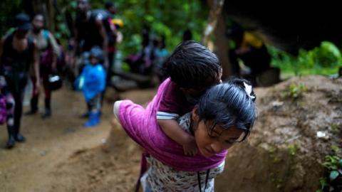 A migrant carries a child as she and others continue their journey to the US border, in Acandi, Colombia, 9 July 2023