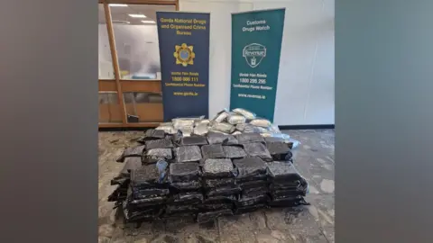 A large quantity of packets of cannabis on a floor with Gardaí signs behind it.