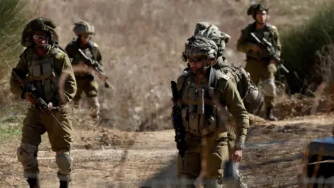 EPA A number of soldiers in camouflage carry guns and wear sunglasses as they walk through some scrubland  