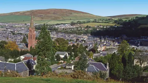 Getty Images A general view of a town surrounded by green hills. There is a church steeple in the left of the picture. 