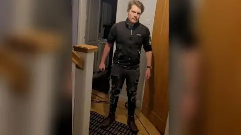 Lancashire Police Jacob Gill stands in front of his victim, staring at him while holding a knife in his hand. He is wearing ripped black jeans and a black top.