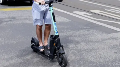 A man in sandals riding an e-scooter.