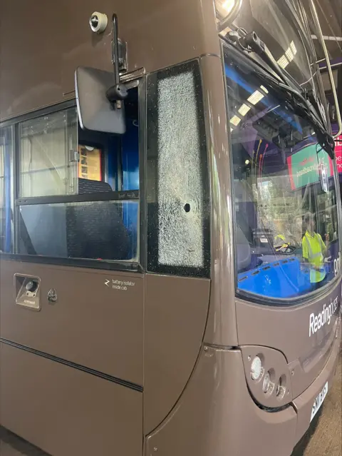 Reading Buses The front of a Reading Bus with the window next to its cockpit shattered, with a noticeable hole (about the size of a nut) 