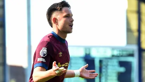 Reuters George Hirst, wearing a burgundy and blue away kit holds his hands out during a match.