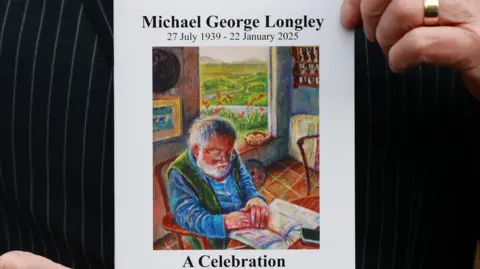 PA Hands holding up the order of service of Michael Longley. It's a painting of him sitting by the table reading a newspaper in the countryside. It says 'Michael Gorge Longley 27 July 1939-22 January 2025 A Celebration Saturday 1st February 12 Noon All Souls Church Elmwood Avenue, Belfast'