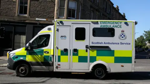 An ambulance passes flats as it is driven along a street