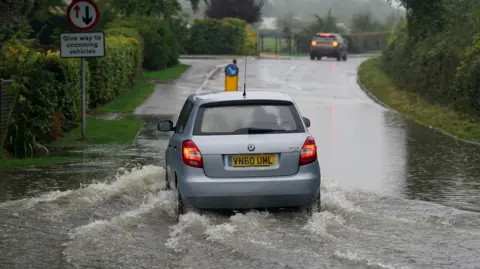 PA A silver car drives through a flooded road in Willersey village, Gloucestershire. 