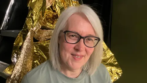 Jane McKnight A woman, pictured from the shoulders up, smiling at the camera. She is wearing a green top and glasses and she has blonde hair. 