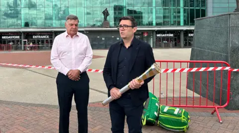 Baton of Hope Sam Allardyce and Andy Burnham, who is holding the Baton of Hope, outside Old Trafford.