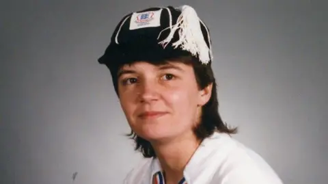 Brighton & Hove Albion FC A close-up image of a woman with short brown hair wearing a white shirt and a black England cap, and she is in front of a grey background.