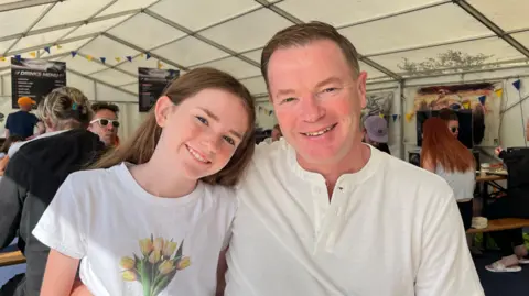 Tom Williams/BBC A young girl and her father sat a table inside a marquee.