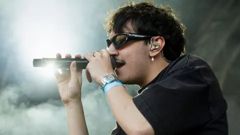 Getty Images Artemas on stage, wearing dark glasses and singing into a microphone, surrounded by dry ice