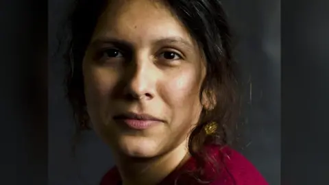 Edinburgh Rape Crisis Centre Mridul Wadhwa, a Scottish Indian trans woman with long brown hair and a magenta top, looks into the camera