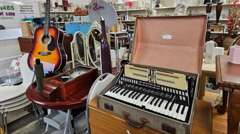 Paul Moseley/BBC A picture of part of the interior of the shop. In the foreground we can see a large accordion in its case. Behind, we 