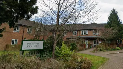 A sign for Beechwood Care Home in Northallerton with the care home building in the background. There are multiple trees around the site.