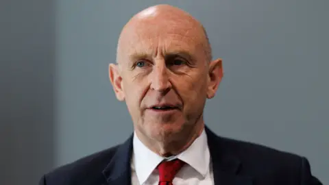 PA Media A bald headed man in a dark suit with a red tie and white shirt