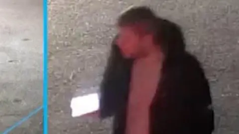 Essex Police A CCTV image of Kyle Pauley taken on the night of the attack. He is wearing a black coat and light coloured jumper. He has a phone in his hand.
