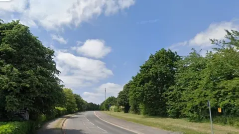 Google maps street view of Great Stoke Way in Stoke Gifford. It is a straight road with pavements either side. A phone mast can be seen in the distance on one side of the road. Trees and bushes are lining both pavements.