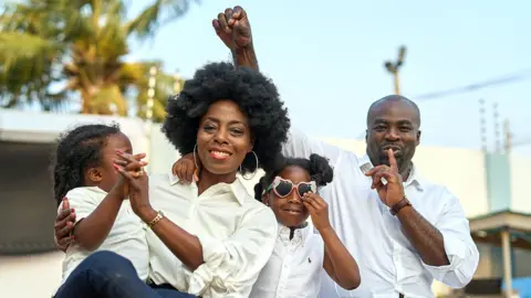 Family Handout Irene with her husband and children posing for a family photo. Her husband cheekily lifts a strand of her hair and puts his finger to his lips, conspiratorially. 