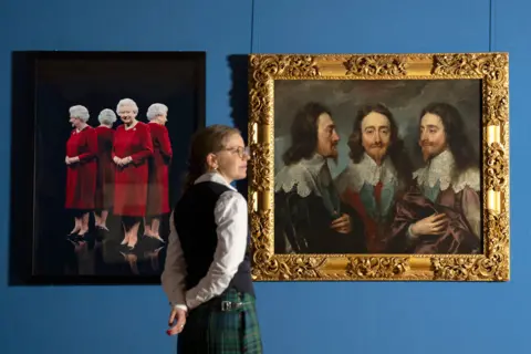 Jane Barlow/PA Wire A curator wearing a kilt and white shirt with black wasitcoat stands next two two paintings - one of the Queen in a red dress and the other of Charles I with long brown hair and pointy beard.