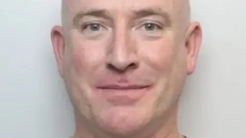 South Yorkshire Police A close-up crop of Martin Underwood's mugshot. He is a bald man. He is smiling without teeth.