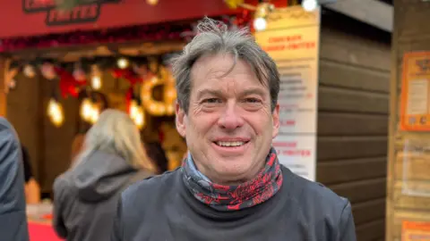 David Miller outside at a Christmas market in casual clothing