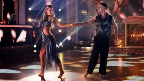 Kyran O'Brien/RTÉ Gymnast Rhys McClenaghan and his dance partner Laura Nolan perform in black outfits and barefoot while holding hands on Dancing with the Stars