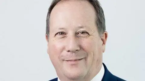 Gov.UK A man smiling into the camera. He has dark hair that is slightly greying.