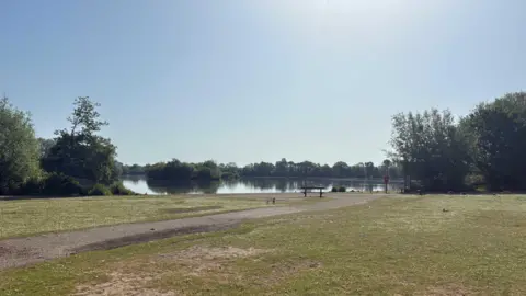 BBC A large park with a lake in the distance. A footpath stretches towards the lake with trees either side and on the far edge of the water.