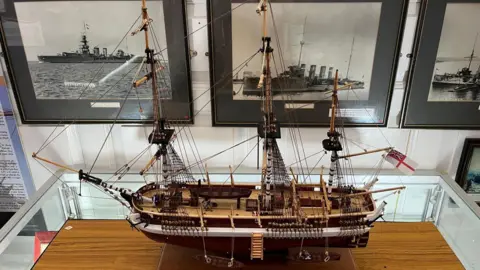 Pembroke Dock Heritage Centre A model of HMS Erebus. It was a large naval ship, made of wood, with large wooden masts and a flag at the back.