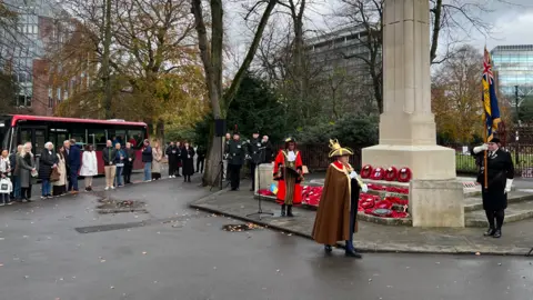 Armistice Day ceremony in Reading with a small group of people watching alongside the war memorial with wreaths of poppies laid on its steps