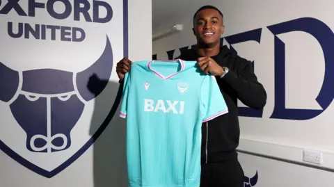 Aidomo Emakhu holds up an Oxford shirt
