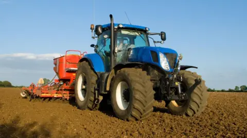Getty Images Farmer driving tractor and drilling seed corn in ploughed field