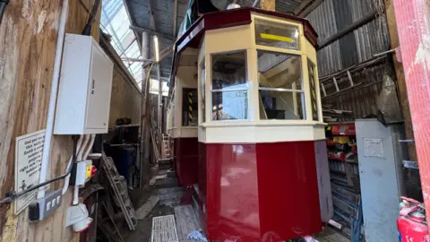 A red and cream tram which has been restored. It sits in a metal and wooden barn