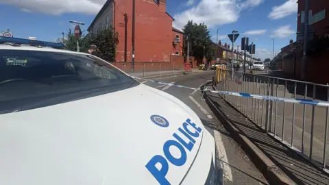 A West Midlands police vehicle at the scene. It is in front of the blue and white police tape.
